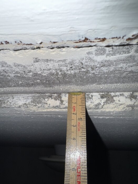 Spår i taket mellan hall och kök, nästan 2 cm djupt, med måttband synligt för jämförelse. Halltaket är lägre än kökstaket.