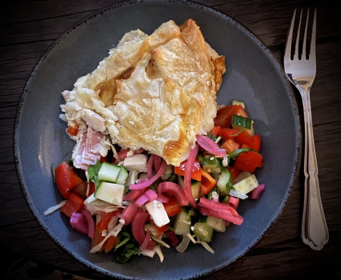 Tallrik med pajrester och sallad inklusive picklad rödlök, serverad med gaffel på en träyta.