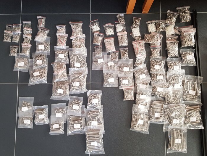 Flera påsar med skruvar och muttrar i olika storlekar och former, ordnade på golvet för hela samlingen av maskinskruvar.