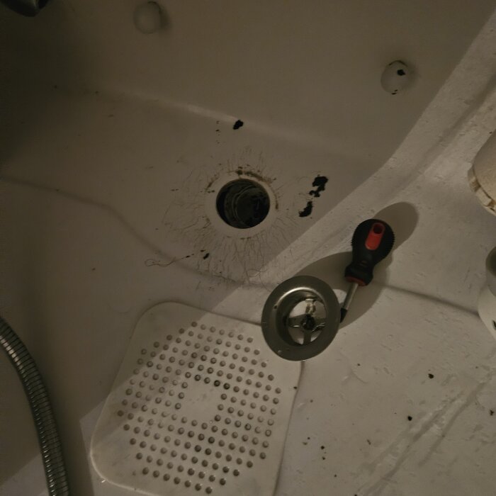Duschgolv med ett avlopp där rören verkar ha lossnat. En skruvmejsel och delar av avloppslocket ligger bredvid på golvet.
