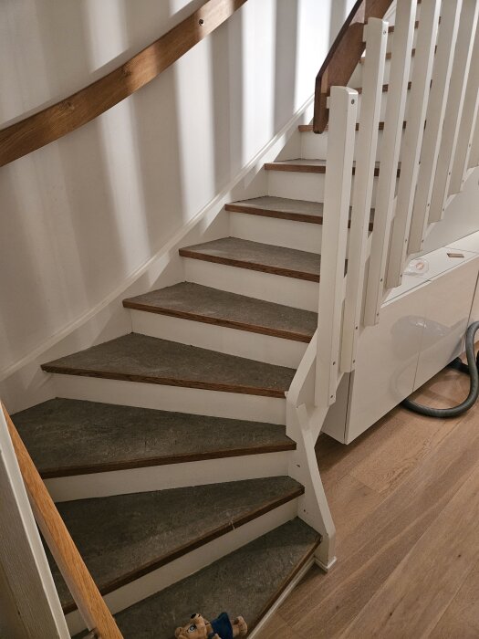 En nyrenoverad trappa med linoleummatta, eklist och vit räcke, projekt under 5000 kr. Ett mjukisdjur ligger vid foten av trappan.