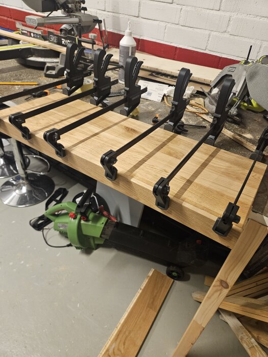 Ekplanka på arbetsbänk fastspänd med flera tvingar, redo för trapprenovering. Verktyg och material syns i bakgrunden.