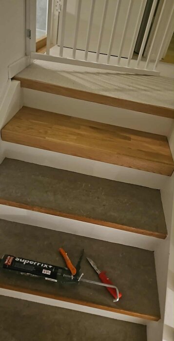 Renoverade trappsteg med eklist, linoleumyta, och redskap som limtub, brytbladskniv och spackelspade på ett av trappstegen.