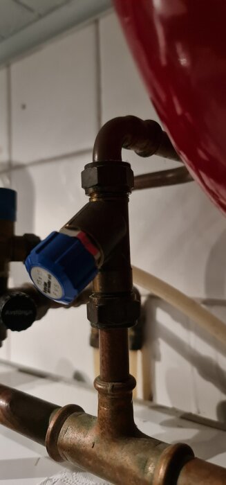 Vattenrör och koppling med blått vred, synlig i en byggnadsmiljö, delvis täckt av ett rött element.