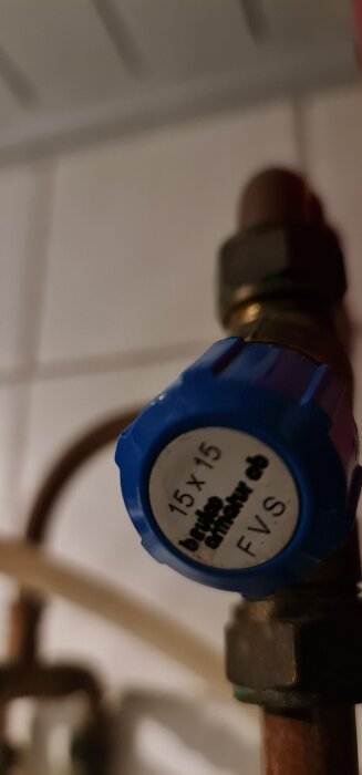 Blå ventil med etikett "15 x 15 brutto armatur ab FVS" på kopparrör i ett rörsystem.