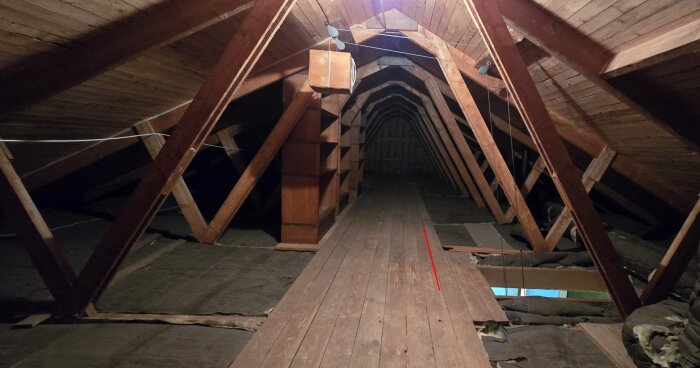 Vind med exponerade träbjälkar och golvbräder, en röd linje markerar en vägg.