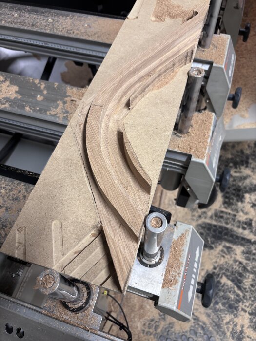 En träskiva på en maskin med en färdigfräst falsad kantlist redo för limning, omgiven av träspån.