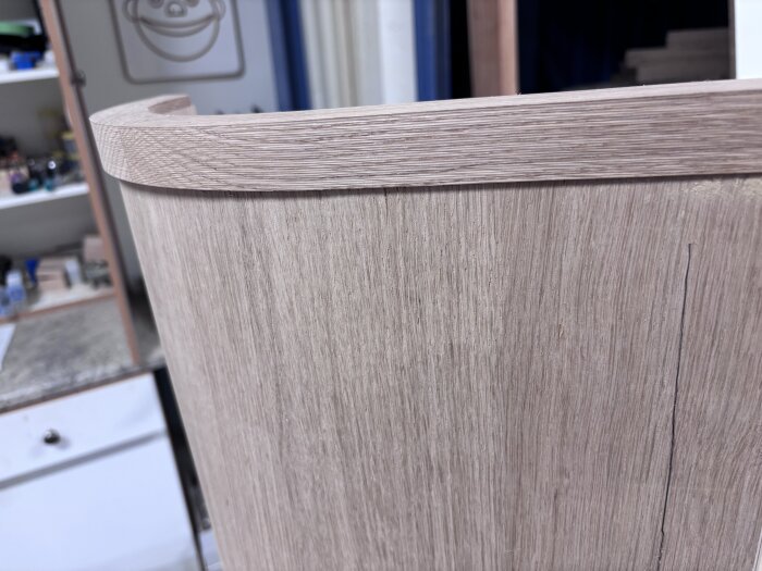 Falsad kantlist gjord av trä, klar för limning, med jämn planhyvlad yta. Bakgrunden visar en verkstadsmiljö med hyllor.