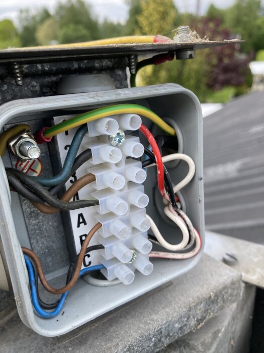 Anslutningsbox på fläktens tak med färgkodade kablar och klämma.