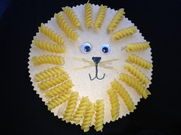 Hantverk av ett lejonansikte, med pasta som man och ögon gjorda av plastrymar.