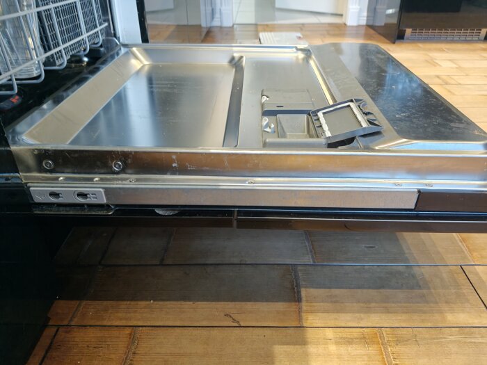 Öppen diskmaskin med synlig metallinsida och panelen delvis borttagen, fokus på avlägsnande av beslag.