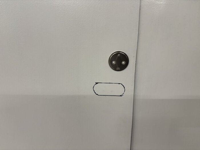Vit dörr med en rostfri del utmarkerad där ett infällnadshandtag ska installeras. Markeringen visar var hålet planeras.