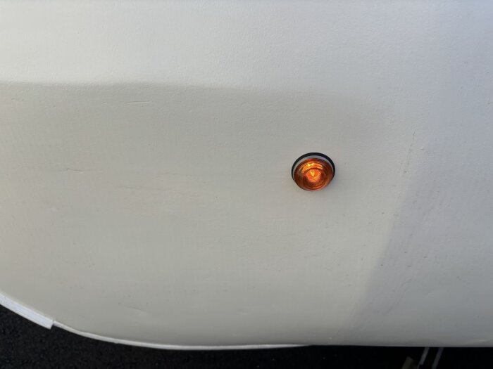 Orange sidoblinkers på vit yta av en husvagn, med rund form och svart gummitätningsring.