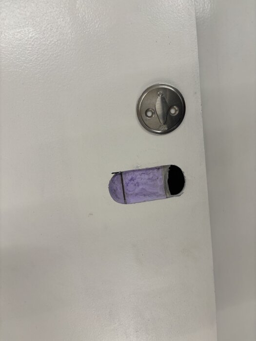 Hål i dörr för installation av infällt handtag, med delvis monterat rostfritt beslag.