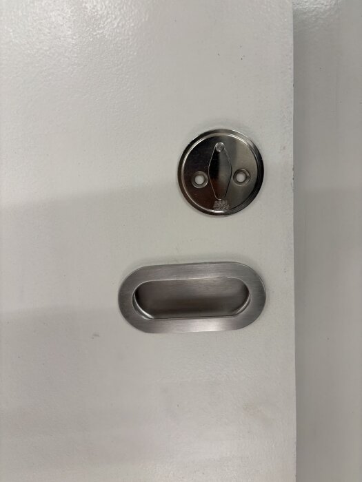 Infällt rostfritt dörrhandtag och skruvar på vit dörr, detaljerad bild av installation i en renoverad husvagn.