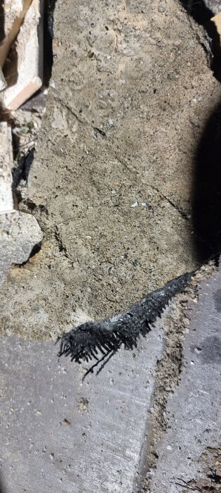 Hårt material med fibrer synligt under ett uppbrutet betonggolv, potentiellt misstänkt för asbest i ett badrumsrenoveringsprojekt.