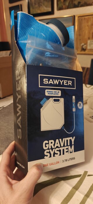 Sawyer Gravity System låda hålls av en hand, innehåller utrustning för vattenfiltrering, som tar bort mikroplast.