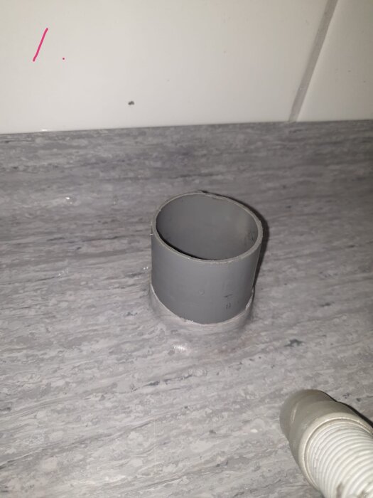 Grått golvrör som möter golvet, eventuellt ojämnt kapat, vilket kan orsaka läckage vid tvättmaskinsutlopp; grå och vit rörkoppling synliga.