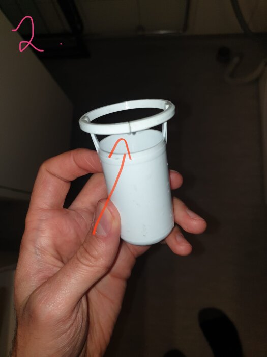 En hand håller ett vitt, cylindriskt vattenlås med en synlig spricka vid övre kanten.