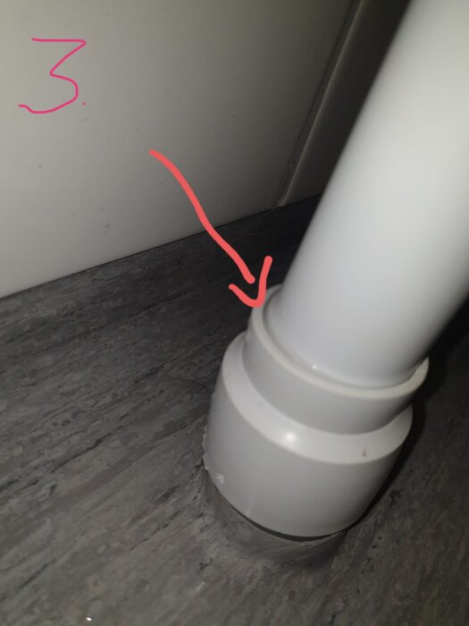 Vit övergång mellan tvättmaskinsutloppsrör och golvrör, markerad som potentiell läckagepunkt med röd pil.