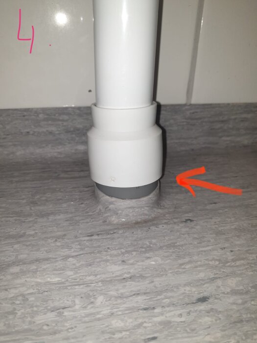 Vitt utloppsrör från tvättmaskin ovanpå grått golvrör, med synlig glipa där vatten kan läcka. Rött streck markerar glipan.