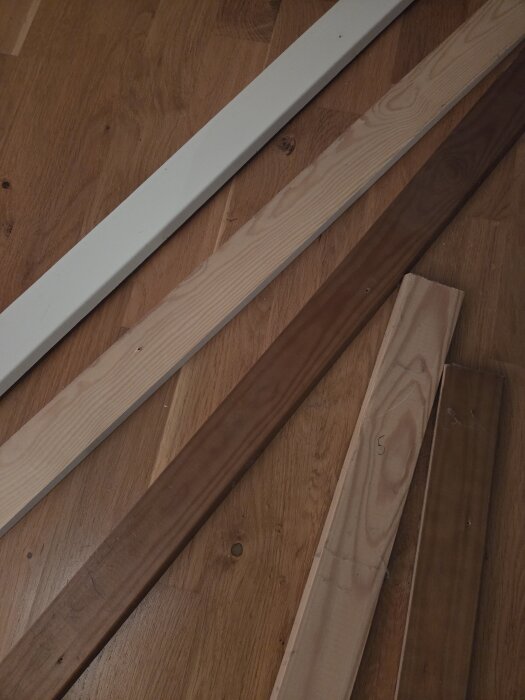 Olika sorters lister liggande på en träyta; två vitmålade, en trären, och två brunbehandlade lister.