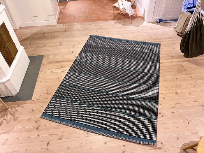 Svart- och vitmönstrad ullmatta från Kasthall Häggå ligger på ett trägolv i ett rum med ljus inredning.