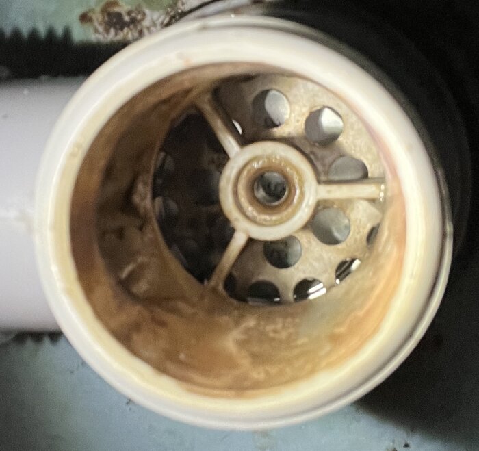 Närbild av insidan på en gammal bottenventil i diskbänken med en central komponent som ser ut som en skruv men snurrar.