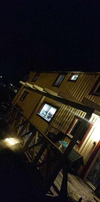 Trähus med verandatak av takreglar, kvällsbild med belysning.