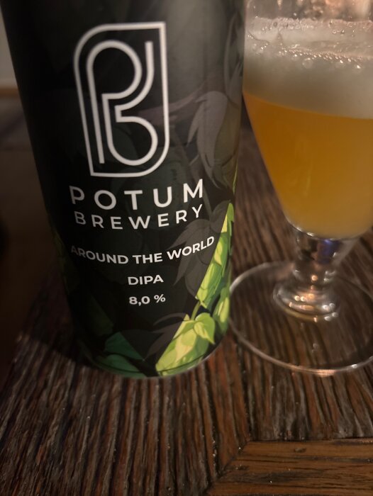 Burk med "Potum Brewery Around the World DIPA 8,0%" och ett glas med öl på ett mörkt träbord.