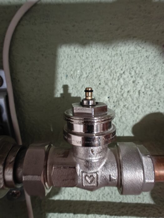 Ventil i närbild med en lös tapp på ovansidan, del av golvvärmesystem i ett pågående renoveringsprojekt.