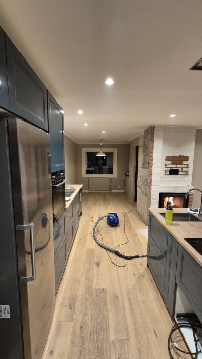 Renovering av kök och vardagsrum med synligt trä- och tegelarbete, samt en dammsugare på golvet.