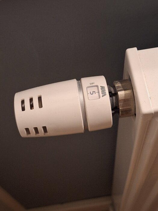 Termostat på radiator inställd på grad 5, monterad på väggen.