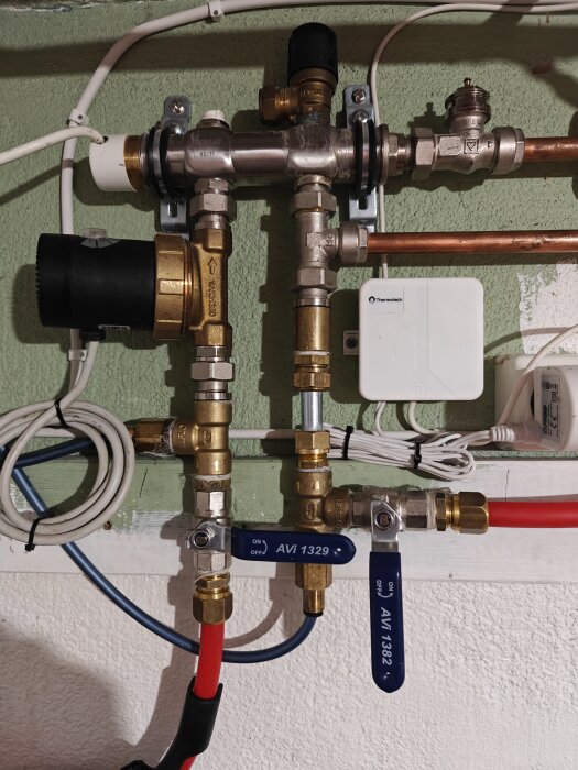 Rörsystem med två röda avstängda slangar, kopplat och avluftat av rörmokare, mot en grön vägg.