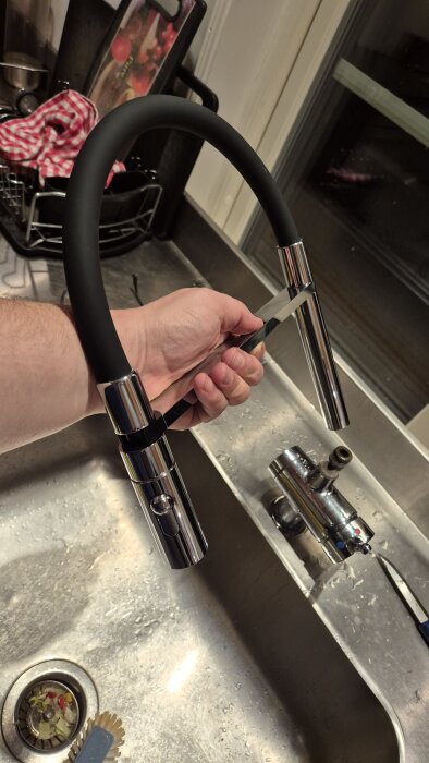 Köksblandare Mora Cera Duo Miniprofi med svart slang och metallmunstycke hålls över diskbänk, bredvid ligger verktyg och diskställ.