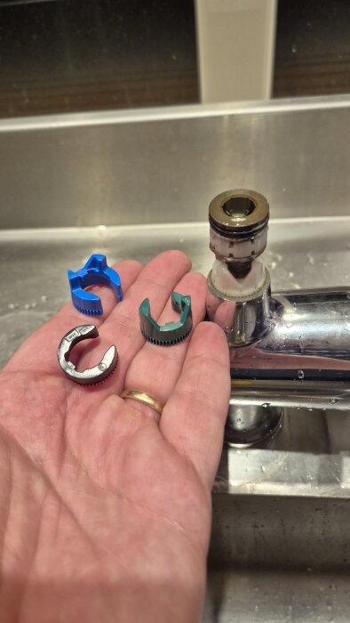 Hand som håller tre färgade plastdelar bredvid en demonterad köksblandare.