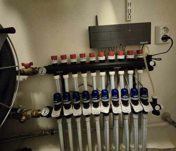 Värmefördelare med röda och blå ventiler samt tryckmätare inom ett värmesystem.