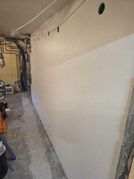 Nymålad vit korridor med eluttag och sladdar i taket, redo för elinstallation och plattsättning av golv.