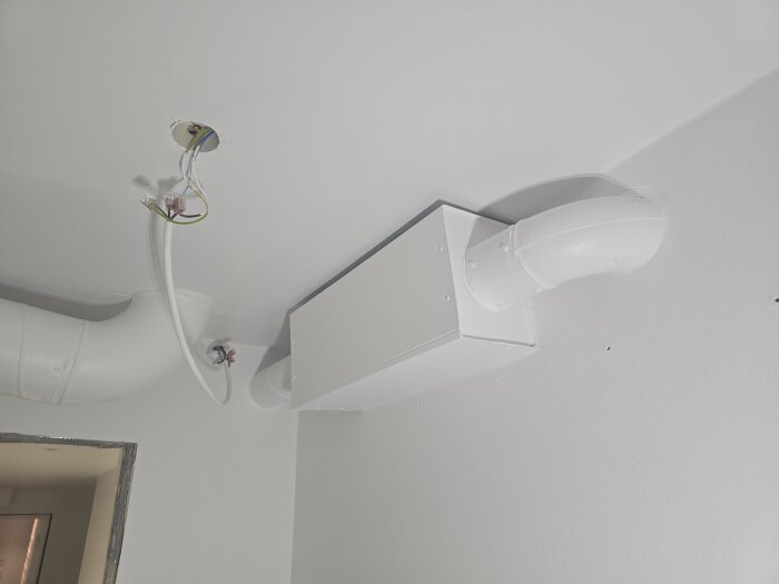 Vitmålad korridor med synliga elektriska kablar och ventilationsrör i taket, redo för installation av takspottar.