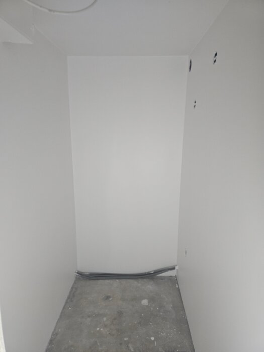 Nymålad vit korridor med synliga kablar och ofärdigt golv, vilket visar en pågående renovering eller byggprojekt.