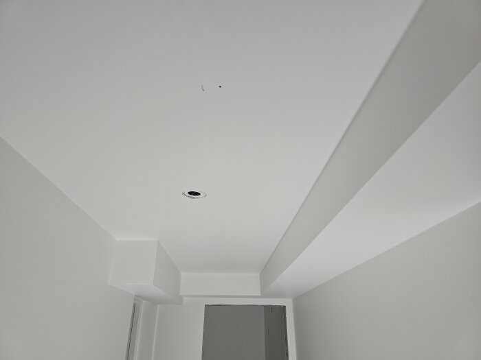 Nymålat vitt tak med ljusmonteringshål i en korridor, redo för elinstallation och infällning av taklampor.