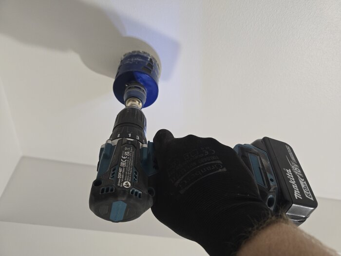 Person borrar hål i tak med en blå borrmaskin för att installera takbelysning.