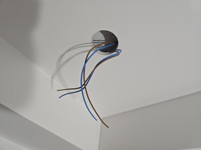 Elektriska kablar hänger från ett runt hål i ett nymålat vitt innertak, redo för installation av takspotlights.