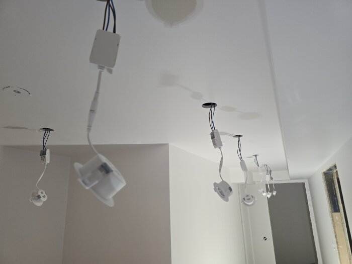 Spotlights för takinstallation hänger i taket i en nymålad korridor, redo för infällning och elanslutning.