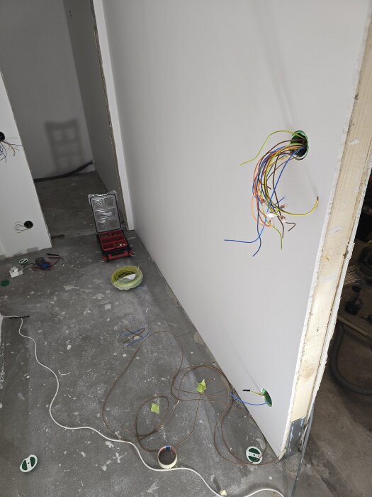 Elektriska kablar sticker ut från en vägg i en nyligen målad korridor som förbereds för elinstallation, med verktyg och material spridda på golvet.
