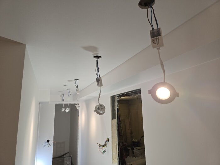 Installering av takbelysning i en nymålad korridor med infällda spottar och hängande sladdar, där en lampa är tänd.