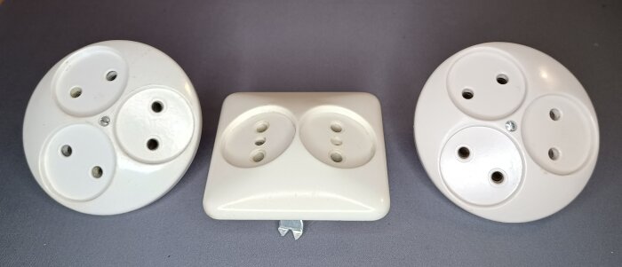 Tre sextio år gamla vita eluttag, ej petskyddade eller jordade, visas på grå bakgrund.