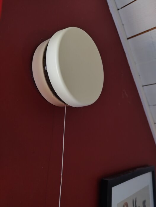 Tilluftsventil på vägg, delvis fastsatt, med vit kåpa och snöre som hänger ner.