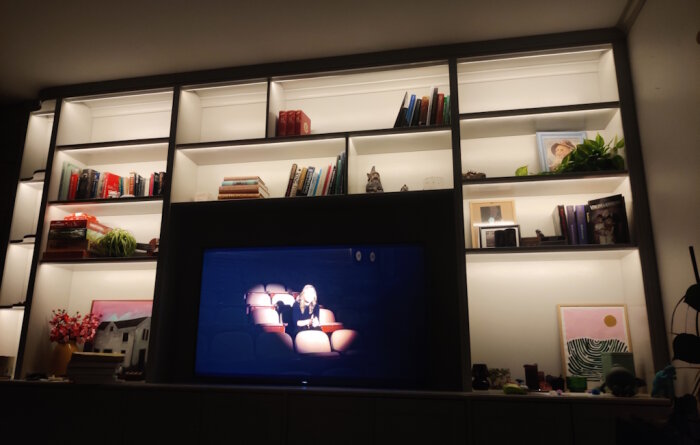 Bokhylla med Ikea Havsta-underdel, egengjord överdel av furu limfog och belysning. TV i mitten och böcker samt dekorationer på hyllor.