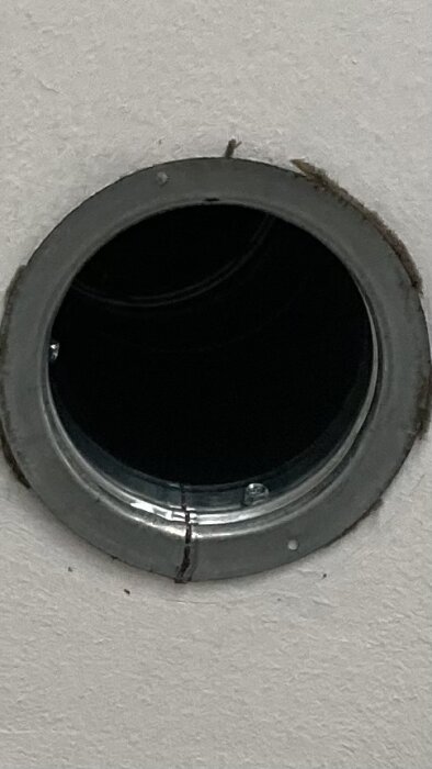 Rund ventilationsöppning i vit vägg med metallram, monterad med två synliga skruvar.